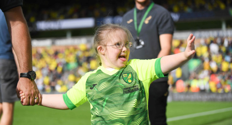 A young girl with down's syndrome smiles and waves