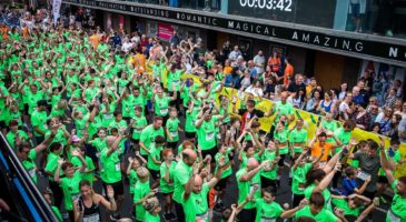group of adult and children in green t-shirts with their arms in the air
